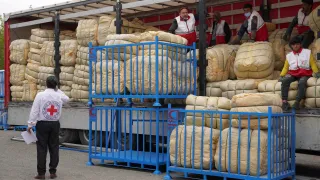 Humanitarian workers unload large bundles of emergency relief supplies from a truck in Iran, with Red Crescent staff coordinating distribution from a loading platform to support people affected by the crisis.