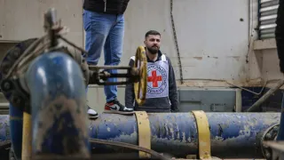 ICRC staff member standing beside large blue water pipes and filtration infrastructure at a water treatment facility in Lebanon, monitoring equipment used to maintain water supply.