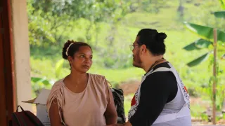Una persona del Comité Internacional de la Cruz Roja conversa con una persona de la comunidad en una zona rural. Ambos están de pie al aire libre, rodeados de vegetación y paisaje campestre.