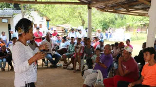 Una persona del Comité Internacional de la Cruz Roja dialoga con miembros de una comunidad reunida, mientras las personas escuchan atentamente la conversación.
