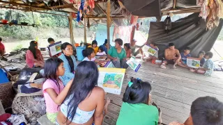 Comunidad indígena en una zona rural de Colombia participa en un taller sobre comportamientos seguros frente a riesgos de artefactos explosivos. Varias personas están sentadas en un salón comunitario, escuchando atentamente una capacitación.