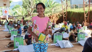 Conflict-affected affected farmer holding donated farming tools, smiling