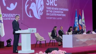 ICRC Vice-President Jürg Lauber speaks at the Third Review Conference of the Convention on Cluster Munitions, with panelists seated on stage and conference branding and flags in the background.