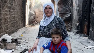 Syria, Aleppo, Jdaideh district. A displaced mother tends to her child and bakes bread in her street alley- merely a block away from the frontline.