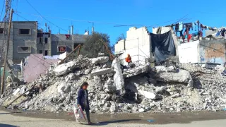 A little girl carrying a bag of supplies walks past destroyed buildings in Rafah, Gaza