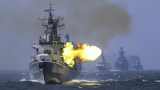 A ship at sea firing artillery while three other ships follow behind.