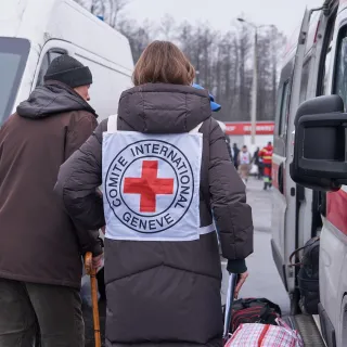 Сотрудница МККК сопровождает пожилого мужчину. 