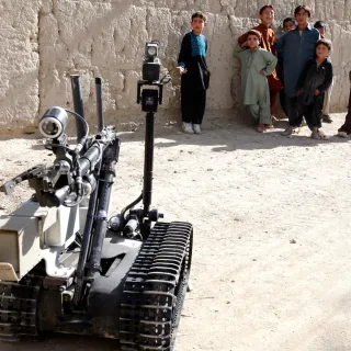 A robot used in war at the foreground while children look on in the background. 