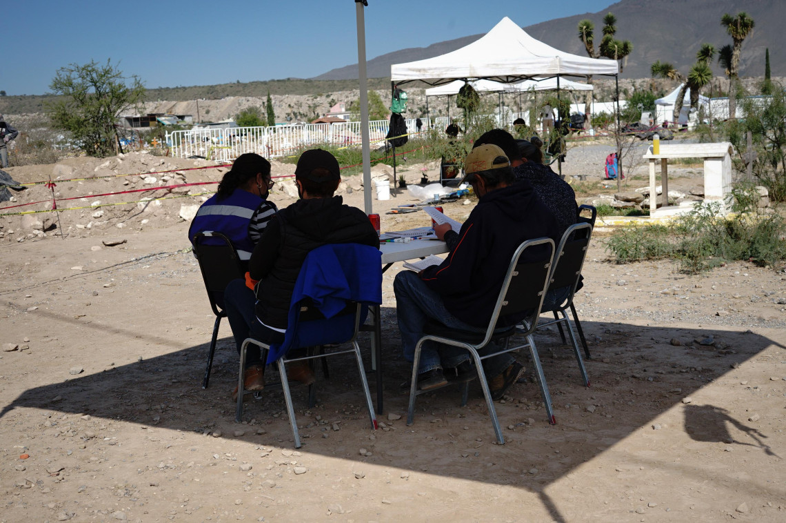 Bajo una carpa para protegerse del sol, las familias se organizan en mesas de trabajo para documentar las exhumaciones