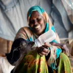 Despite the severe drought, a woman saves up her food to feed a lamb milk from a bottle in an internally displaced persons camp in Somalia.
