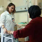 A woman sitting in a hospital bed holds a walker while talking to a female ICRC doctor 