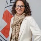 Mulher sorri para a câmera ao lado de uma bandeira com o logotipo do CICV.