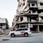 ICRC land cruiser in Homs, Syria, driving past a collapsed building