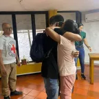 Dos personas se abrazan, mientras otras dos personas presencian el momento de reencuentro