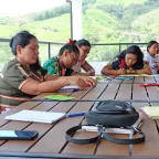 Siete mujeres están sentadas en una mesa, escribiendo y reflexionando