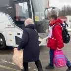 Сотрудник МККК сопровождает женщину с вещами к автобусу. 