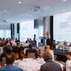 Group of search practioners and experts from various sectors in a conference room with a speaker on the stage