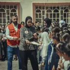 Two ICRC staff members interact with a group of primary school children. Some of the children are reading leaflets