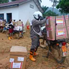 Des travailleurs humanitaires chargent de grandes boîtes de matériel médical sur des motos devant un centre de santé rural, en préparation pour la livraison d’aide dans des zones reculées