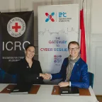 Head of ICRC Global Cyber Hub shaking hands with the CEO of Luxembourg House of Cybersecurity in front of the roll-ups of the respective organizations. With the flags of the European Union and Luxembourg next to the roll-ups.