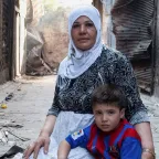 Syria, Aleppo, Jdaideh district. A displaced mother tends to her child and bakes bread in her street alley- merely a block away from the frontline.