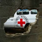Emblem on the side of ICRC vehicle seen through a hole in a brick wall