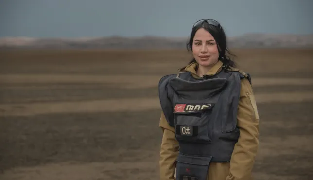 Noora Murad wearing protective gear looks at the camera from a mine field in Iraq.
