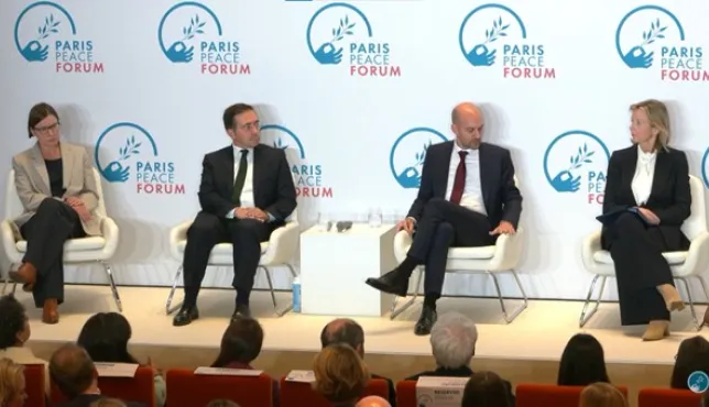 The panelists sit on stage at the Paris Peace Forum, engaged in discussion. They are seated on white chairs in front of a backdrop displaying the Paris Peace Forum logo. The audience is visible in the foreground.
