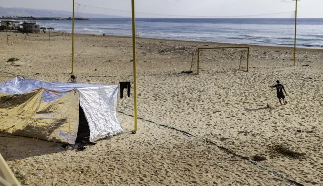 A boy plays football on the beach along the Corniche in Beirut, Lebanon, on March 7, 2026, next to a tent set up by a displaced family who had to move from Beirut’s southern suburbs following an evacuation order issued by Israel.