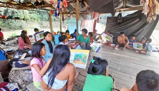 Comunidad indígena en una zona rural de Colombia participa en un taller sobre comportamientos seguros frente a riesgos de artefactos explosivos. Varias personas están sentadas en un salón comunitario, escuchando atentamente una capacitación.