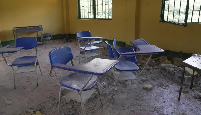 Interior of a classroom at a school in Chocó, Colombia, affected by the August 10 earthquake. Desks are scattered around the room, with debris and pieces of construction material covering parts of the floor due to structural damage.