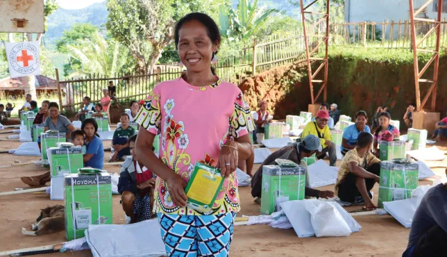 Conflict-affected affected farmer holding donated farming tools, smiling