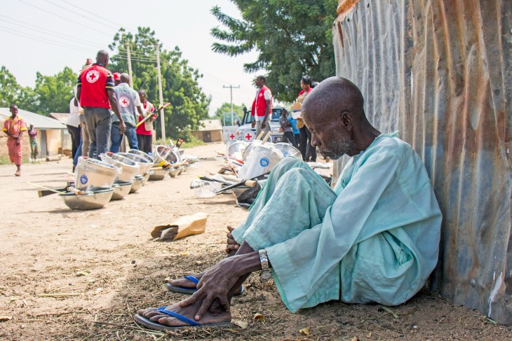 Adana Dilya waits as Nigeria Red Cross and ICRC staff prepare to distribute farming implements to people who have returned from displacement.