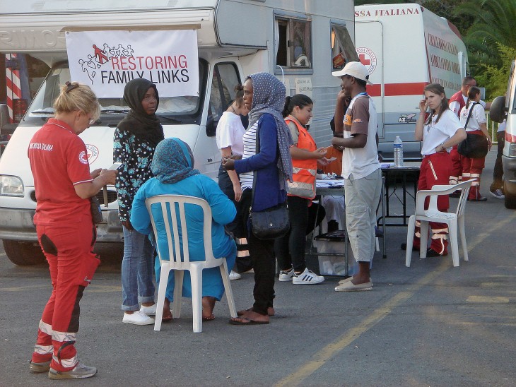 A migrant at an Italian Red Cross aid point talks to his family, while others wait their turn. 